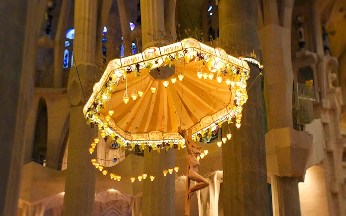 Jesus on cross beneath illuminated umbrella inside Sagrada Familia, Barcelona.