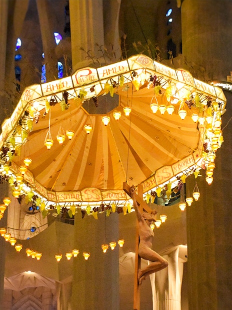 Jesus on cross beneath illuminated umbrella inside Sagrada Familia, Barcelona.