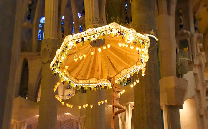 Jesus on cross beneath illuminated umbrella inside Sagrada Familia, Barcelona.