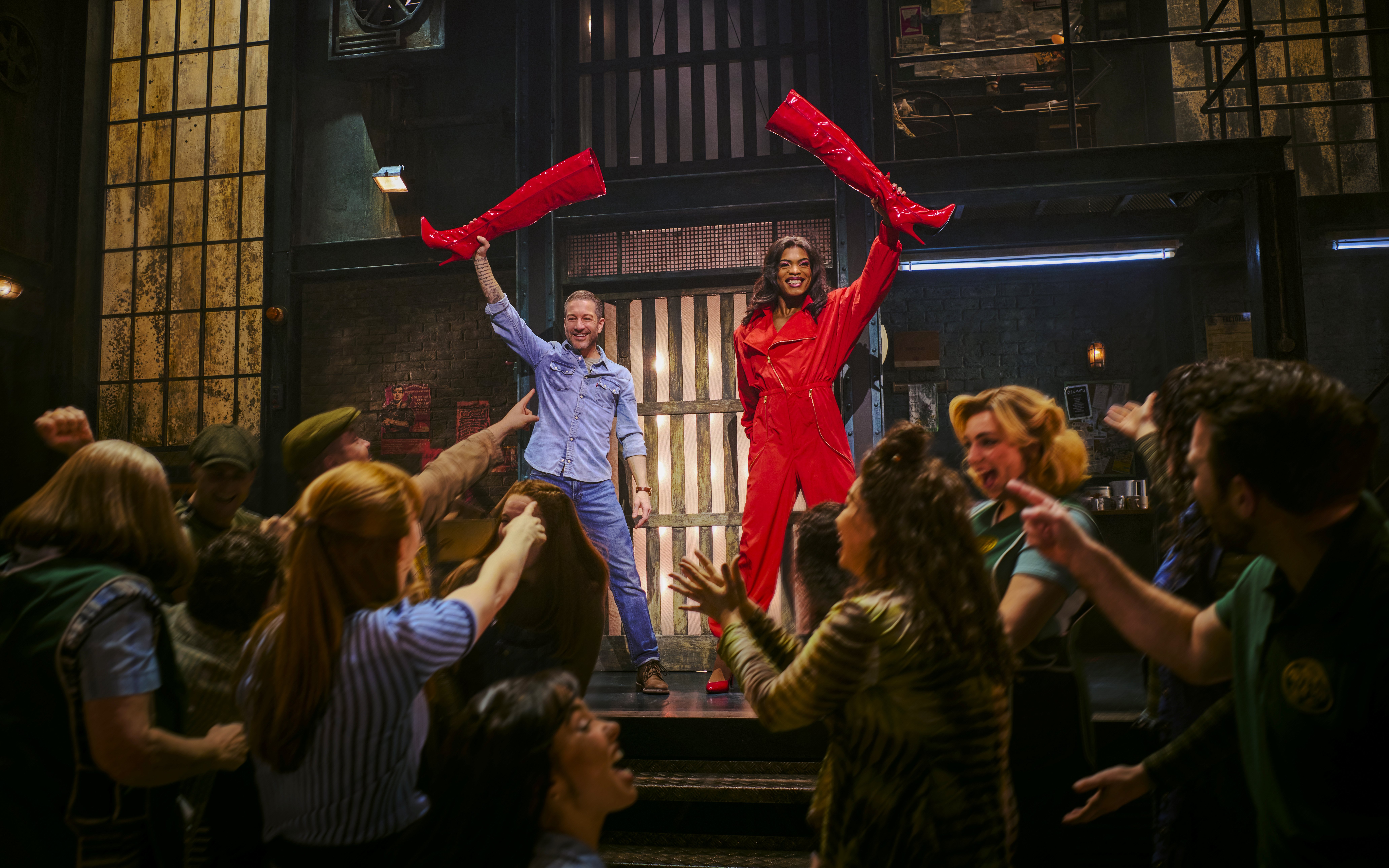 Performers holding red boots on stage during Kinky Boots production.