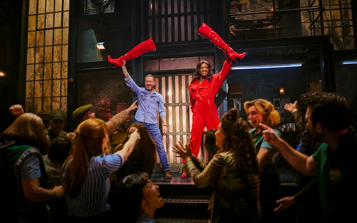 Performers holding red boots on stage during Kinky Boots production.