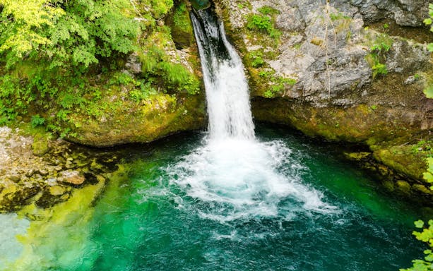 Waterfall flowing into the vibrant blue waters of the Blue Eye spring in Albania.