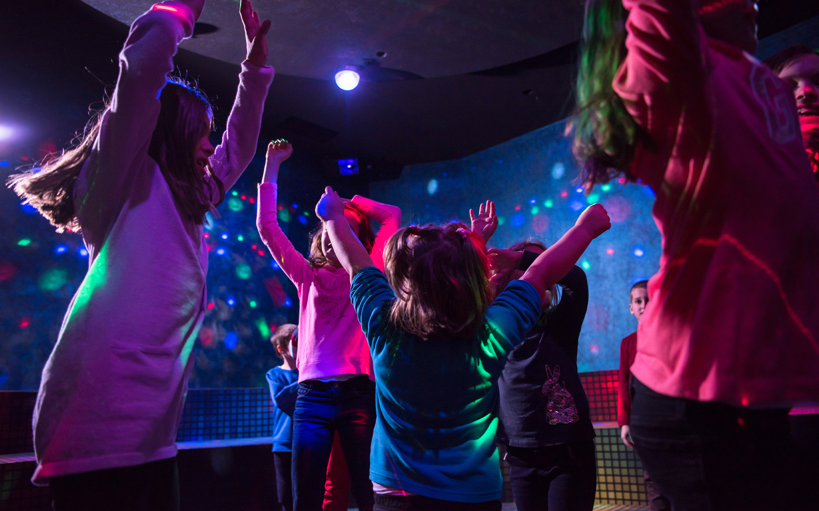 Children dancing under colorful lights at an indoor event.