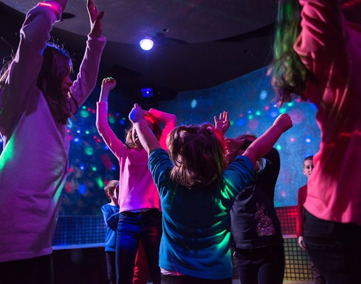 Children dancing under colorful lights at an indoor event.