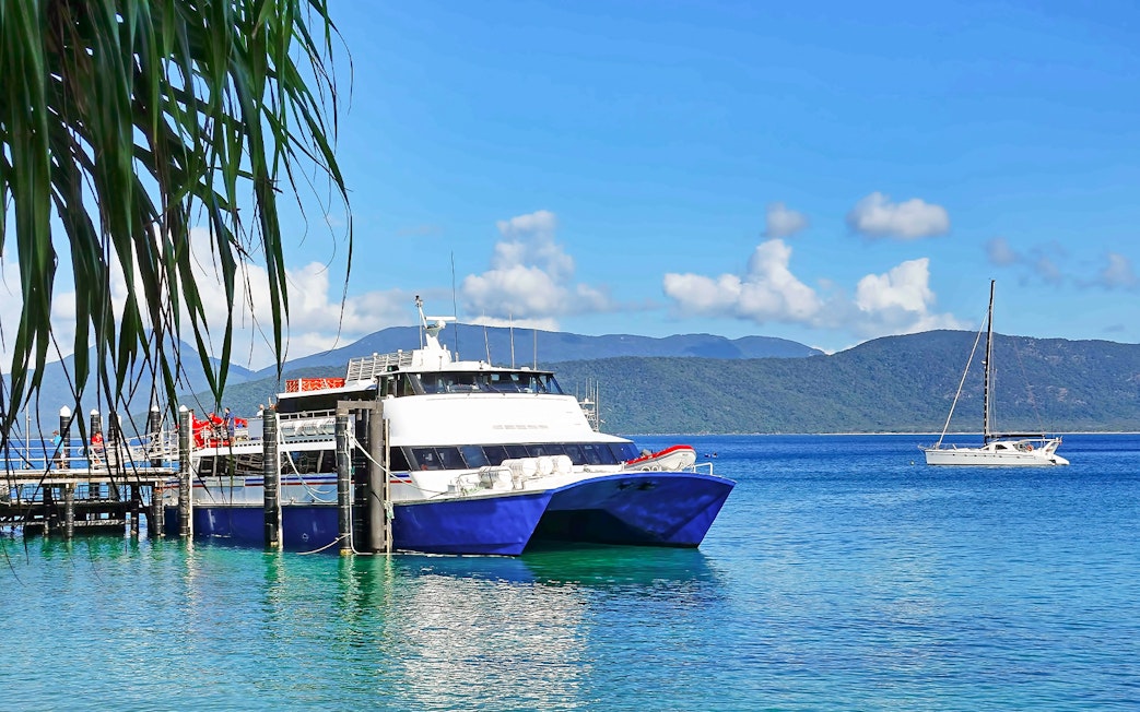 Tourists boarding a boat at Fitzroy Island pier, with lush hills and clear waters, Australia.