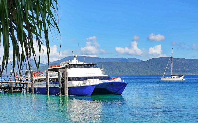 Tourists boarding a boat at Fitzroy Island pier, with lush hills and clear waters, Australia.