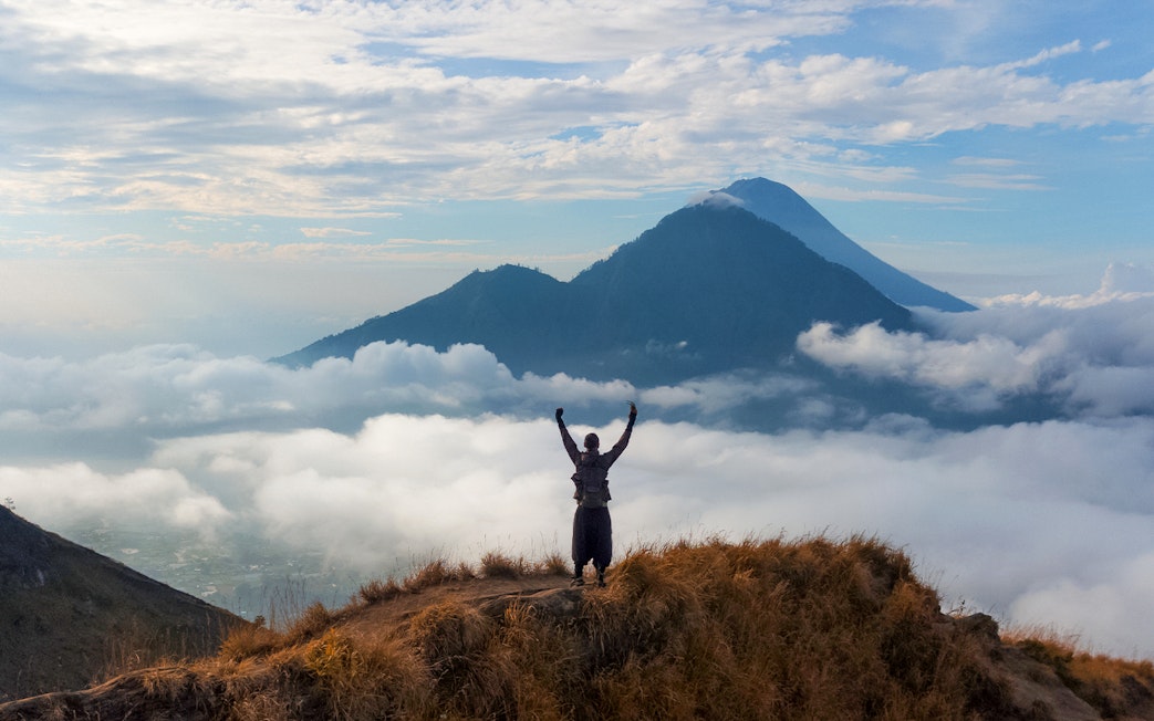Man raising arms while viewing Mount Batur during sunrise trek in Bali.