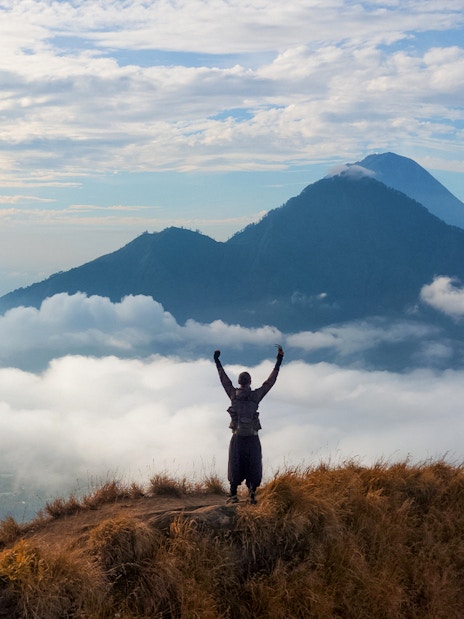 Man raising arms while viewing Mount Batur during sunrise trek in Bali.