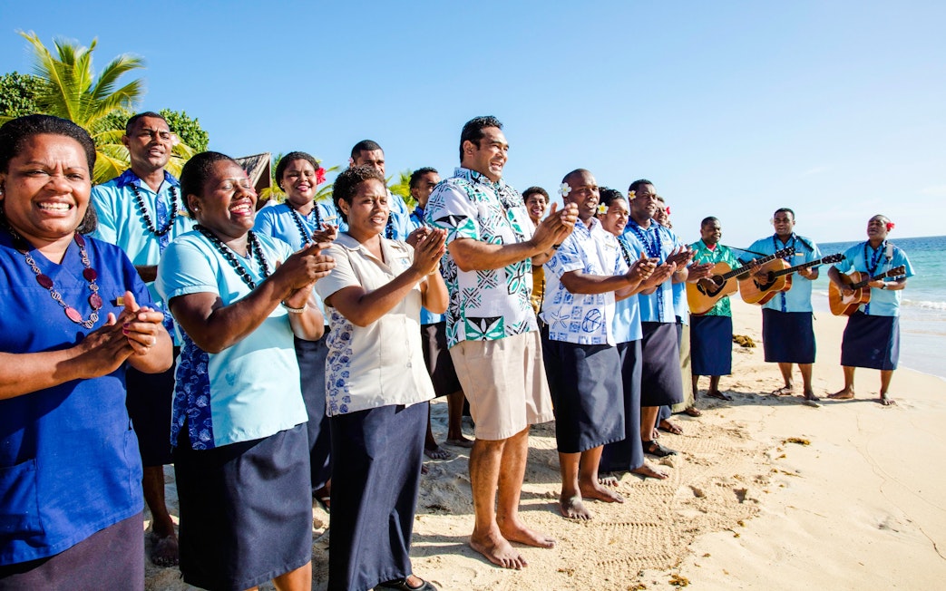 Staff members singing and clapping for guests on Castaway Island, Fiji beach.
