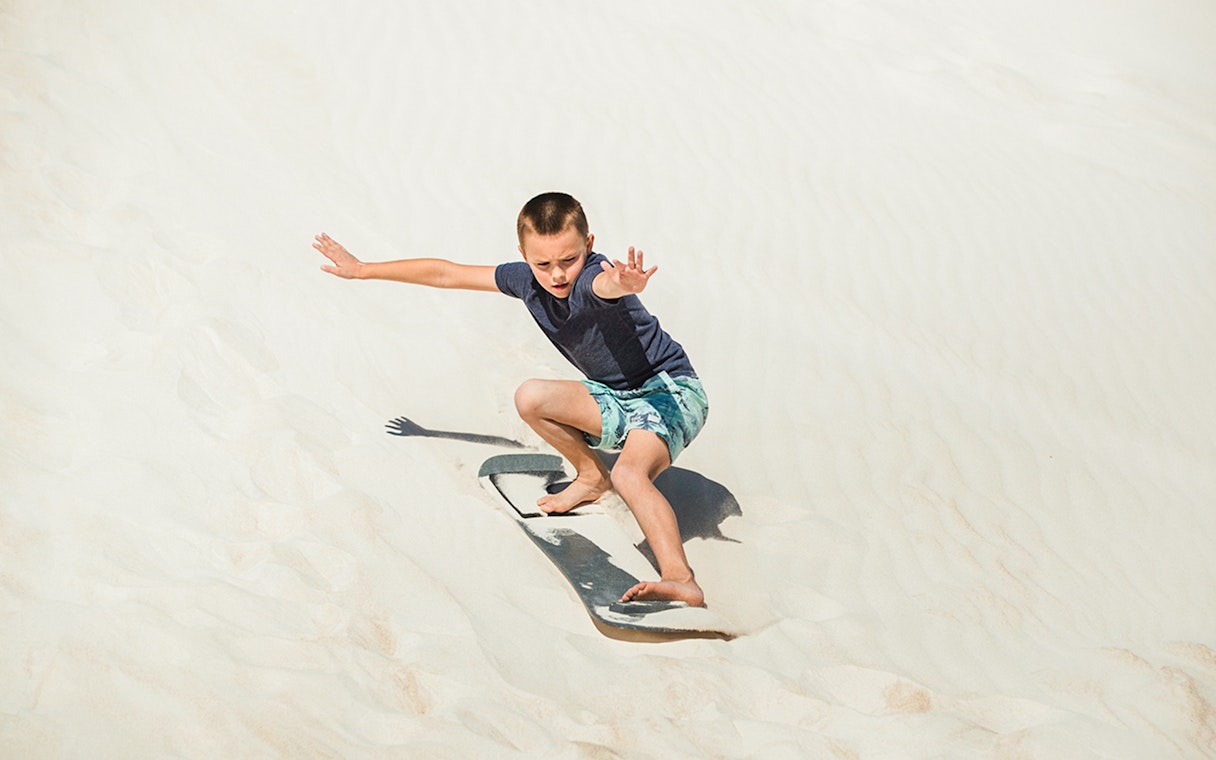 Child sandboarding on dunes in Australia.