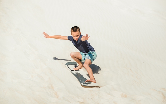 Child sandboarding on dunes in Australia.