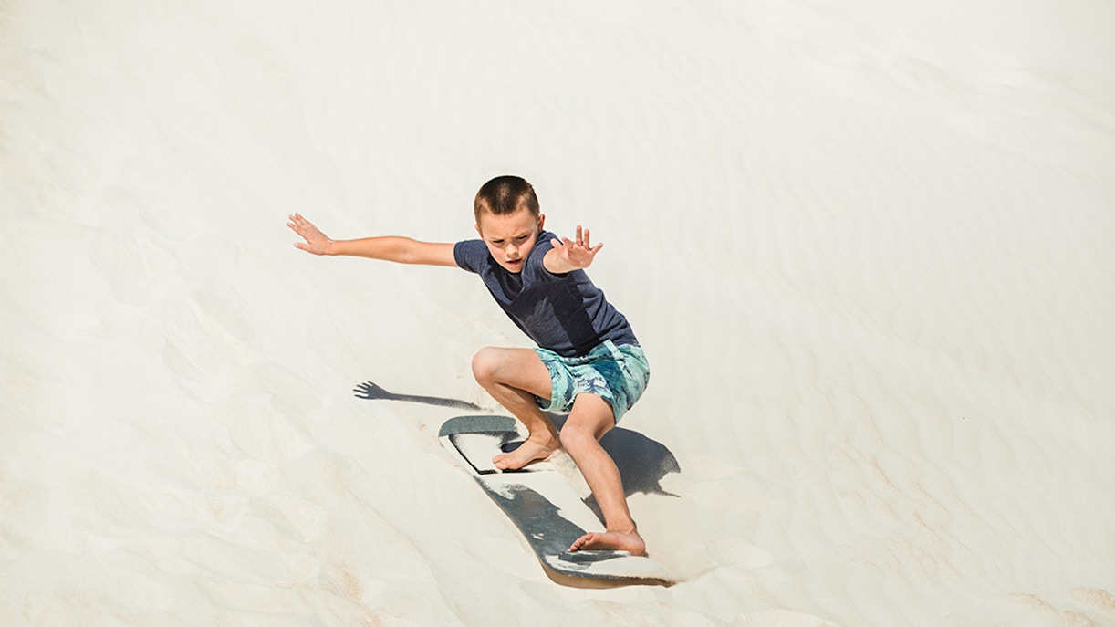 Child sand-boarding on dunes in Australia.