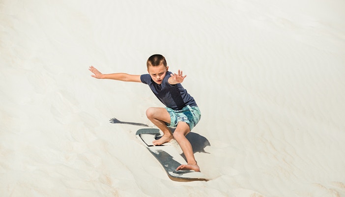 Child sandboarding on dunes in Australia.