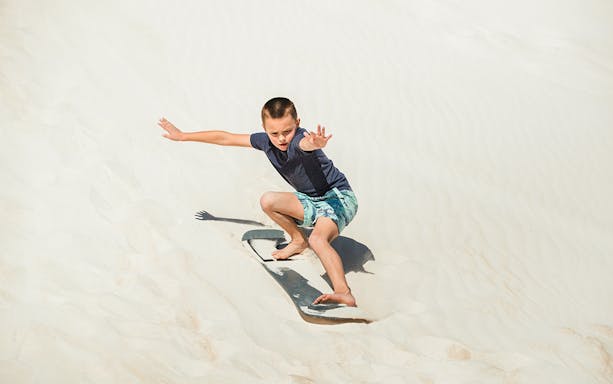 Child sandboarding on dunes in Australia.