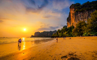 Sunset view of a beach in Krabi with limestone cliffs and people walking along the shore.