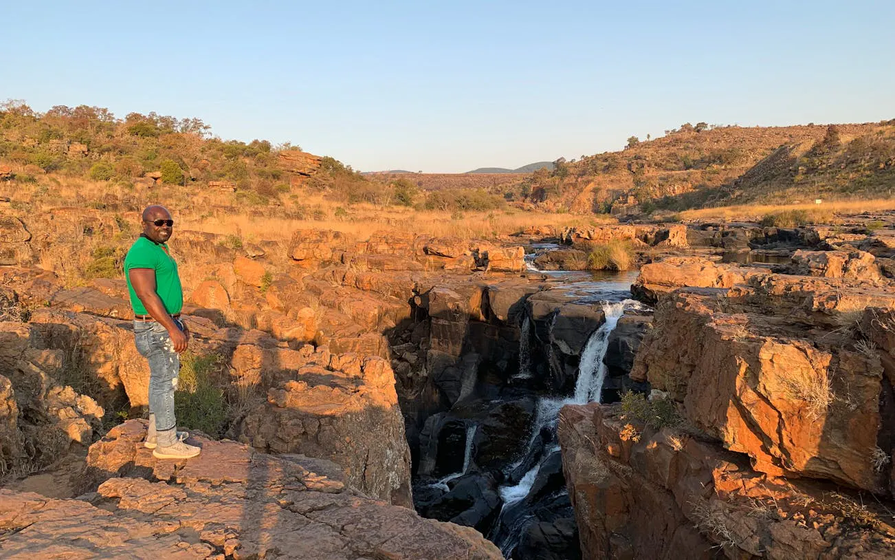 Man standing on rocky cliff overlooking waterfall on Panorama Route, South Africa.