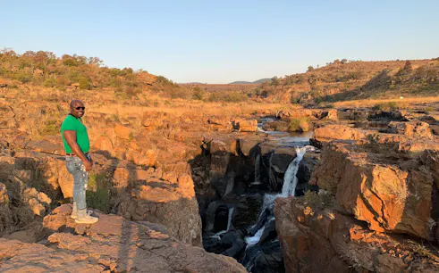 Man standing on rocky cliff overlooking waterfall on Panorama Route, South Africa.