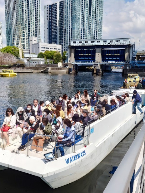 Passengers boarding a cruise boat on the Meguro River in Tokyo with cityscape in the background.