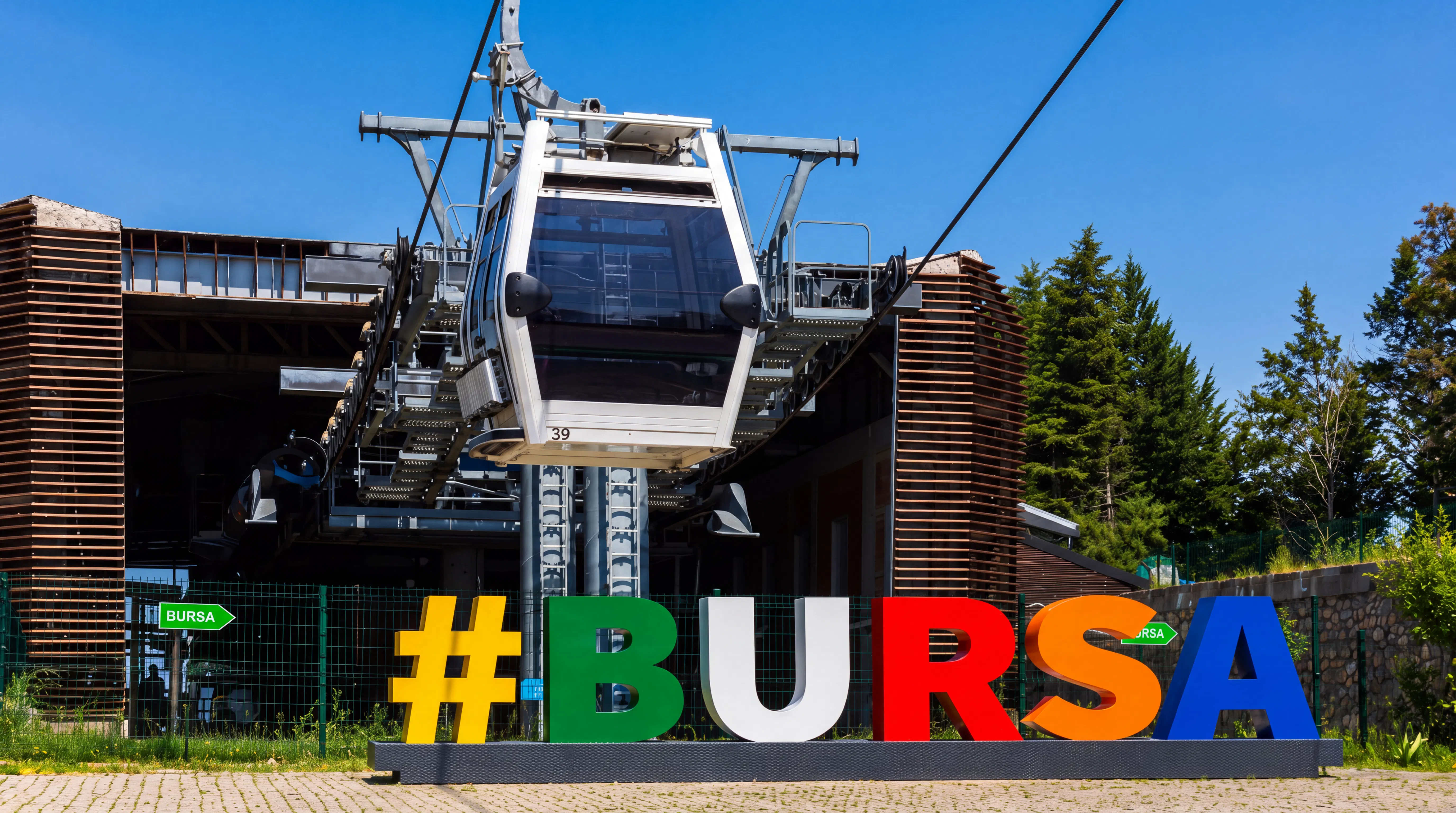Bursa cable car station with colorful sign and trees in the background.