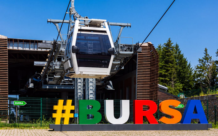 Bursa cable car station with colorful sign and trees in the background.