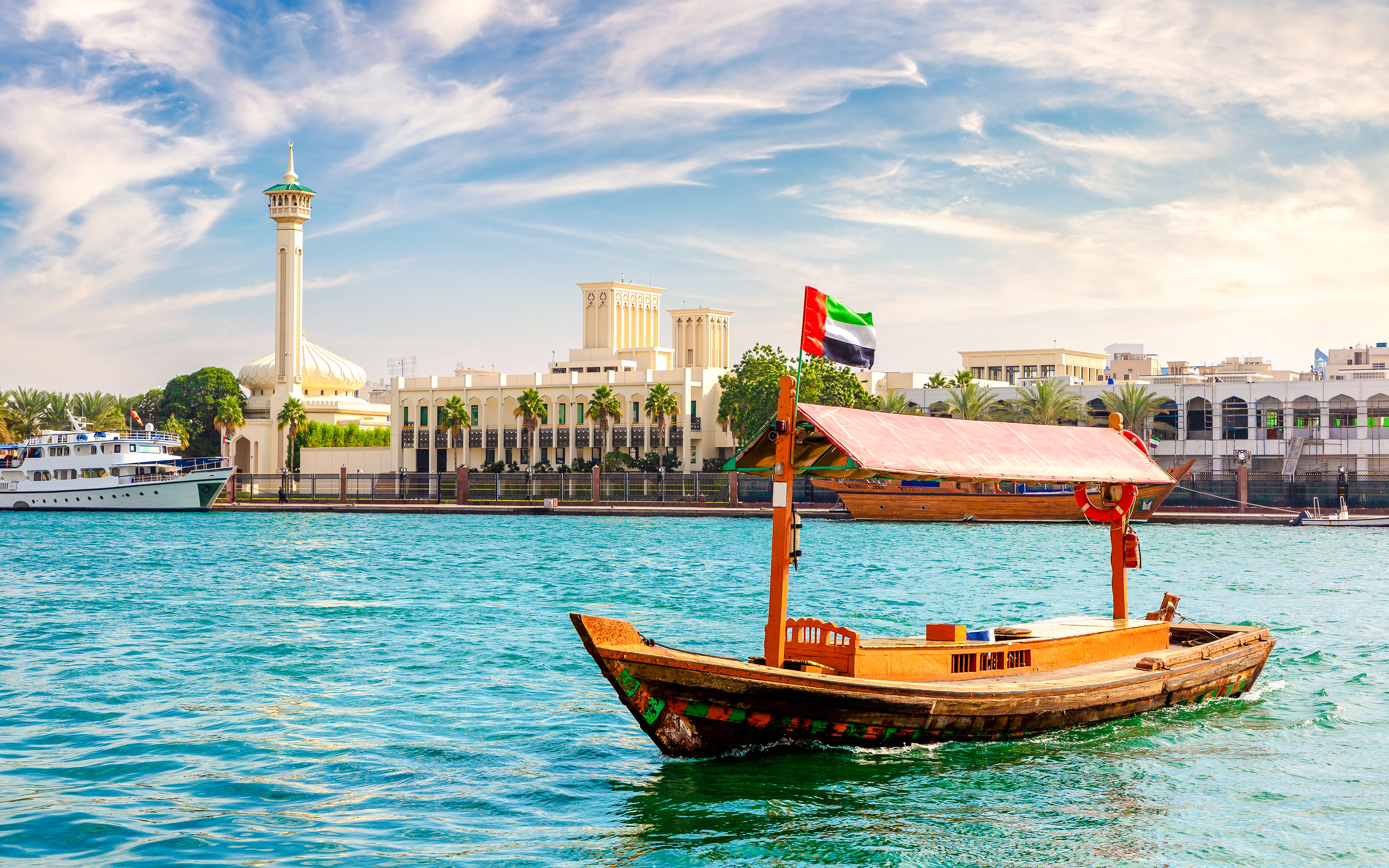 Abra wooden boat on Dubai Creek with cityscape in the background.