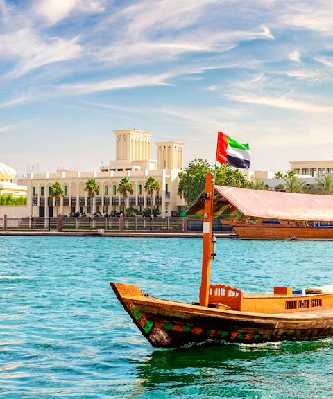 Abra wooden boat on Dubai Creek with cityscape in the background.