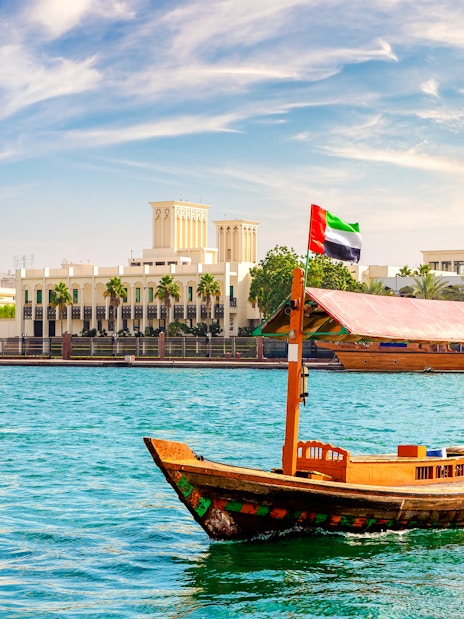 Abra wooden boat on Dubai Creek with cityscape in the background.