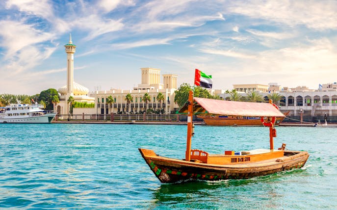 Abra wooden boat on Dubai Creek with cityscape in the background.