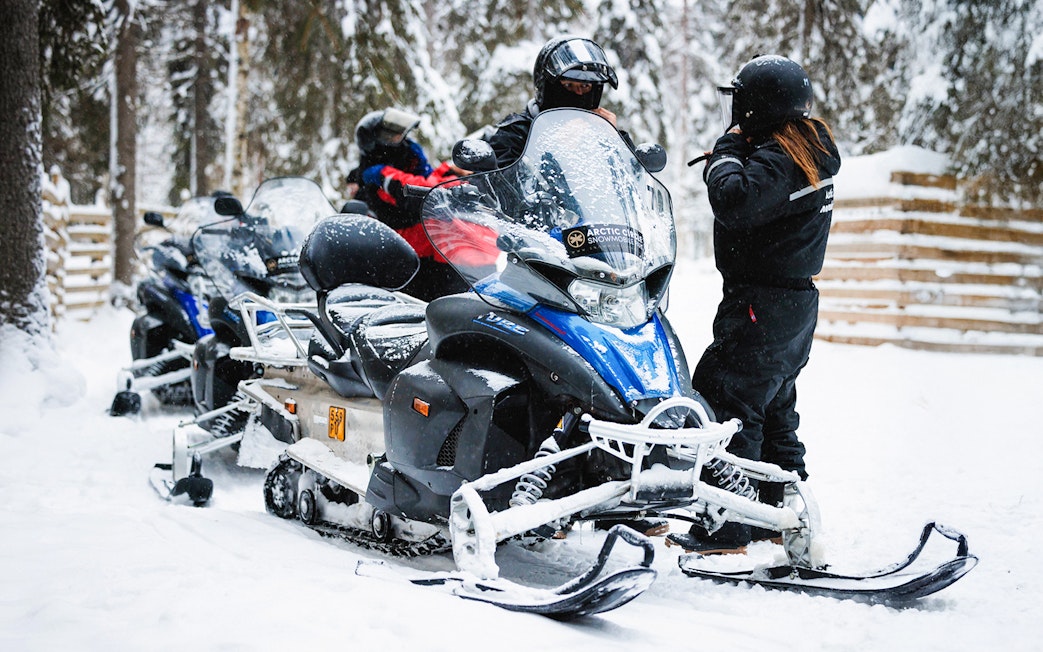 Snowmobiles parked in snowy Lapland forest with riders preparing for a tour.