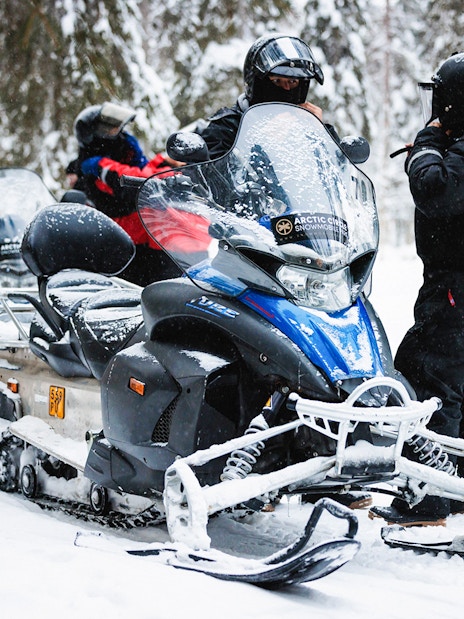 Snowmobiles parked in snowy Lapland forest with riders preparing for a tour.