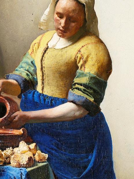 Milkmaid pouring milk into a bowl beside bread and pottery in a rustic kitchen.