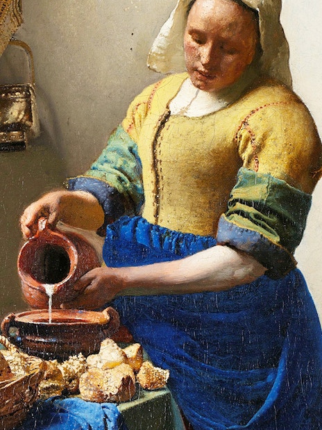 Milkmaid pouring milk into a bowl beside bread and pottery in a rustic kitchen.