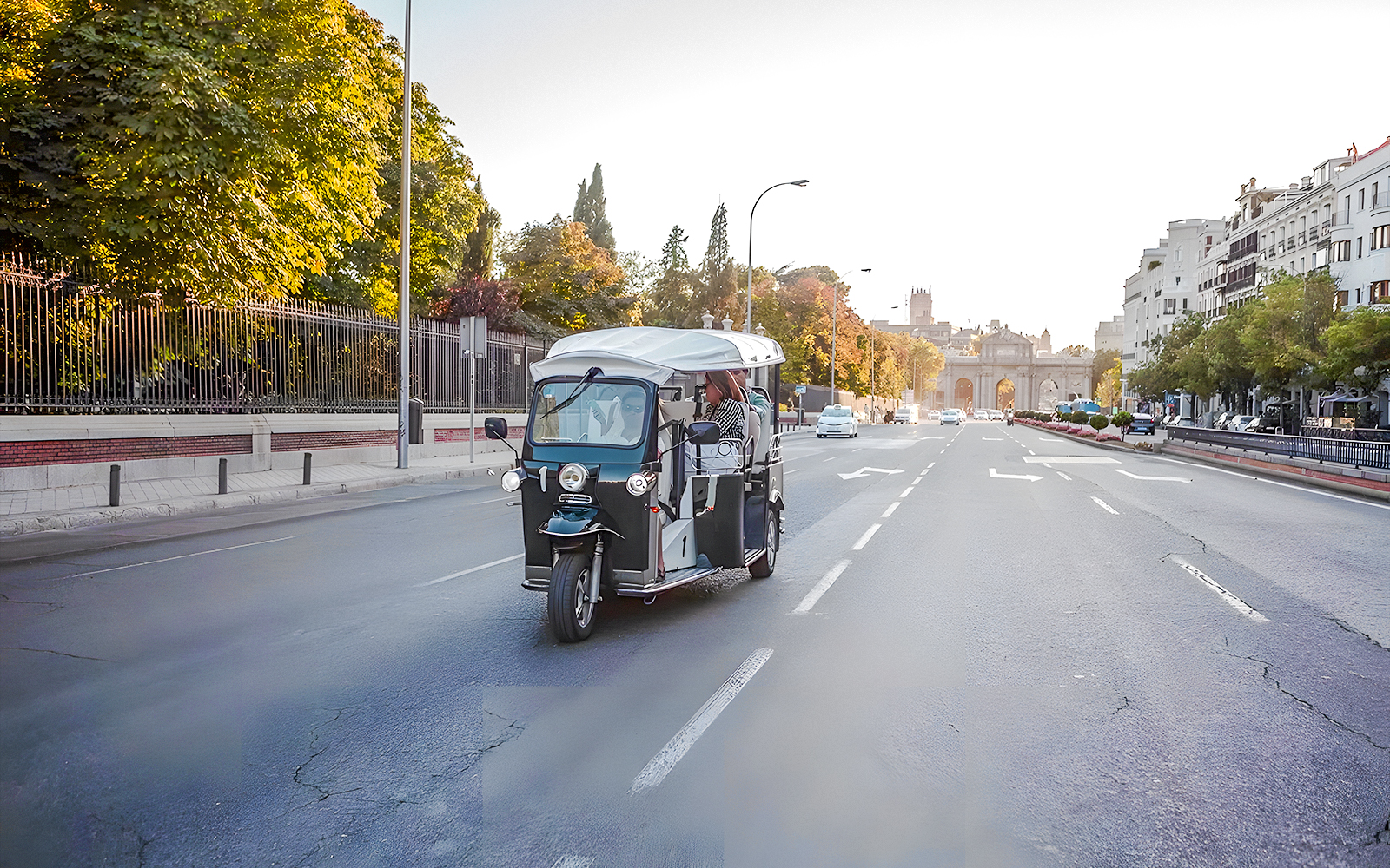 Electric tuk-tuk on a Madrid street with Puerta de Alcalá in the background.