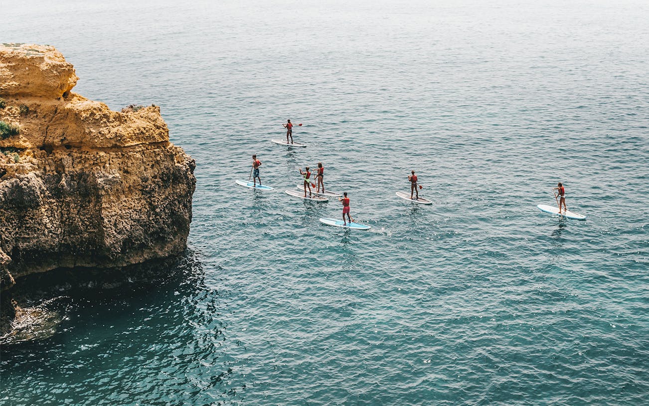 Paddleboarders near cliffs on a Stand-Up Paddle Tour in Polignano a Mare, Italy.