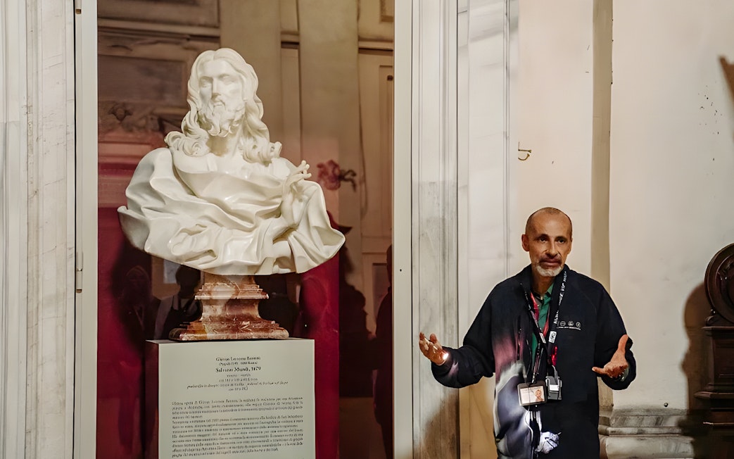 Guide explaining a marble bust in the Basilica of San Nicola during a Roman Catacombs tour.