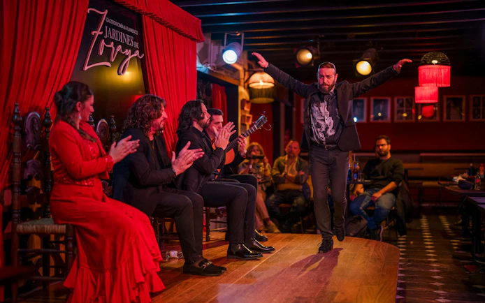 Flamenco dancer performing at Tablao Jardines de Zoraya with musicians clapping.