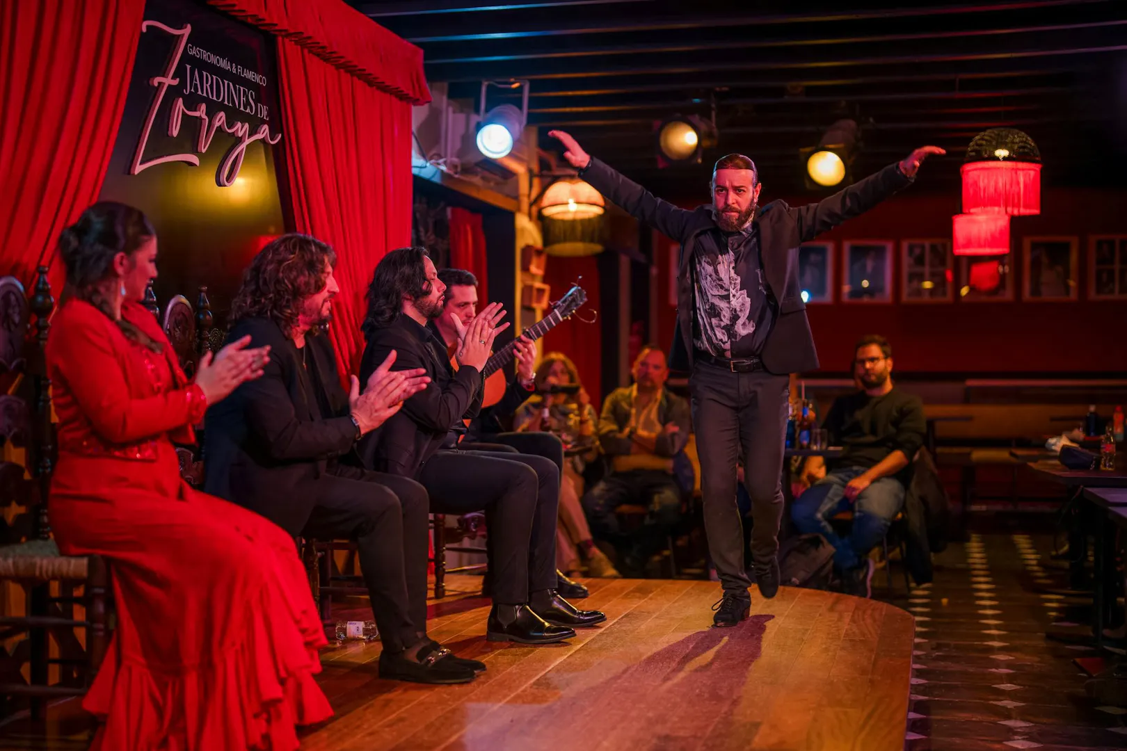 Flamenco dancer performing at Tablao Jardines de Zoraya with musicians clapping.