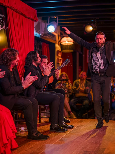 Flamenco dancer performing at Tablao Jardines de Zoraya with musicians clapping.