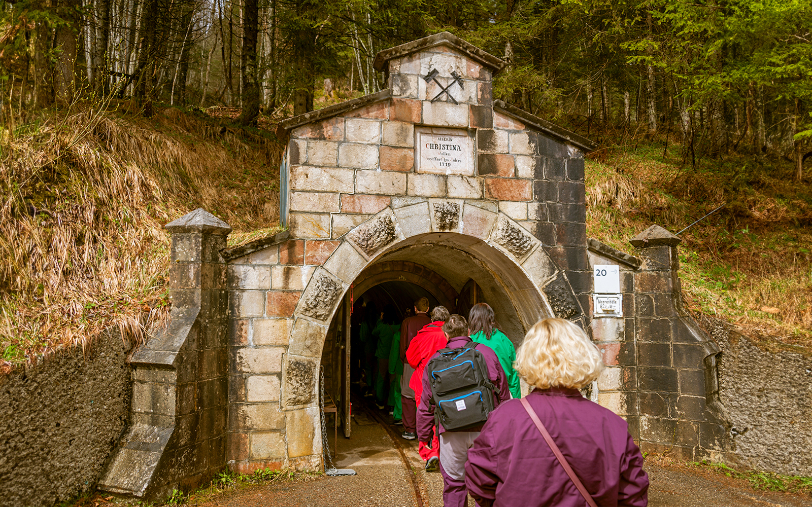 Visitors entering Salzwelten salt mines through stone archway in forest setting.