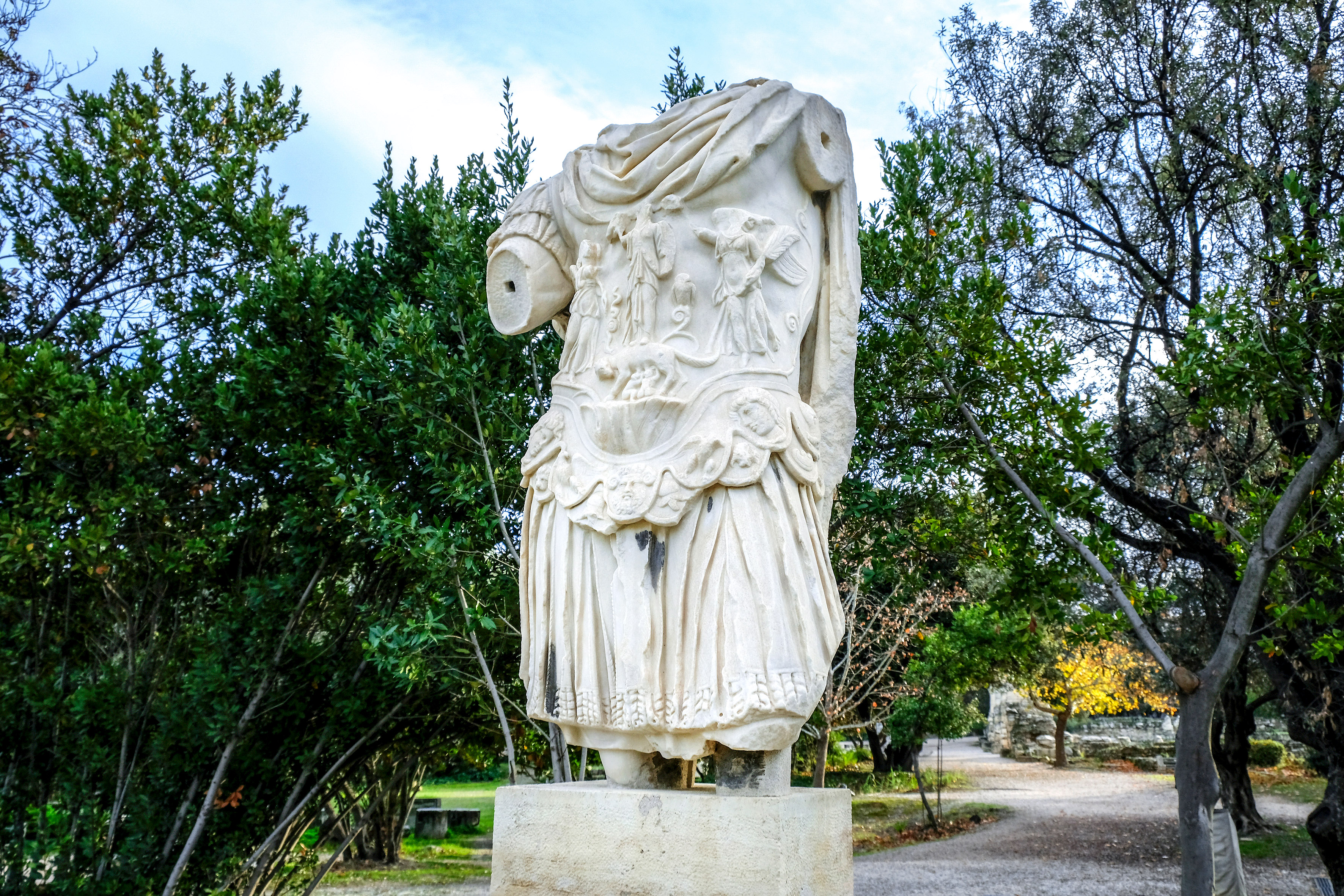 Statue of Emperor Hadrian at the ancient Agora of Athens with surrounding ruins.