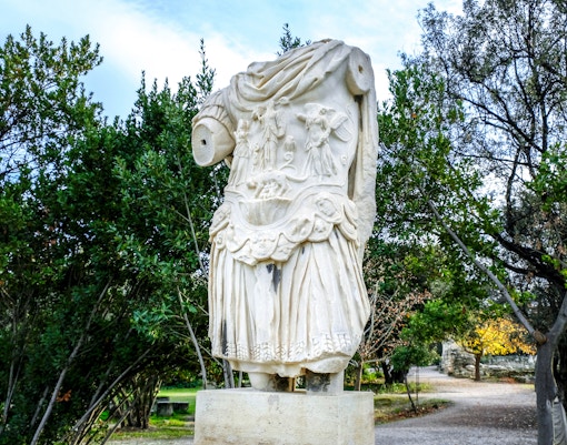 Statue of Emperor Hadrian at the ancient Agora of Athens with surrounding ruins.