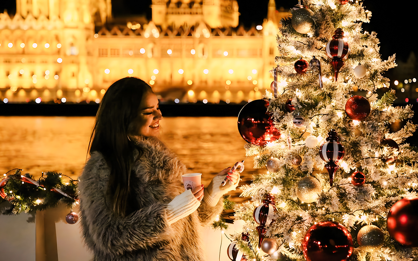 Woman enjoying Christmas Market Cruise in Budapest with decorated tree and illuminated background.