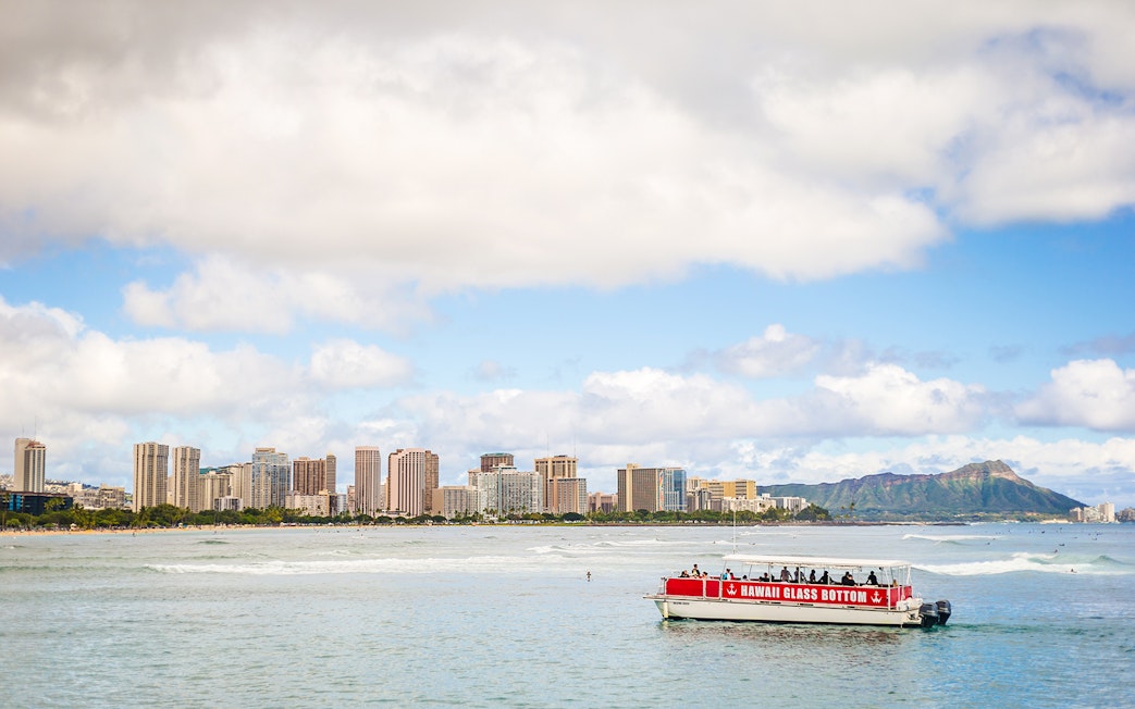 Glass-bottom boat on water with Honolulu skyline and Diamond Head in the background, Hawaii.