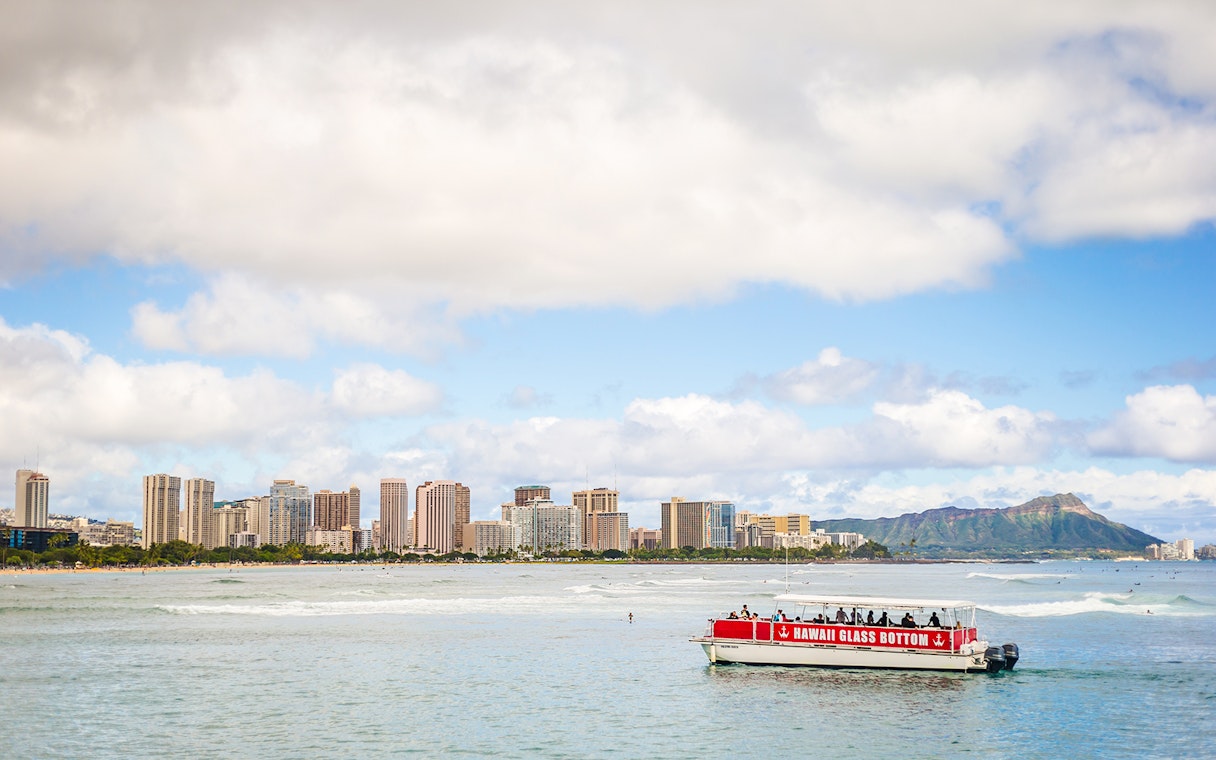 Glass-bottom boat on water with Honolulu skyline and Diamond Head in the background, Hawaii.