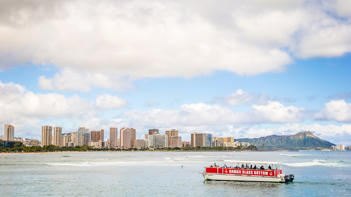 Glass-bottom boat on water with Honolulu skyline and Diamond Head in the background, Hawaii.