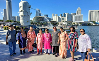 Group of tourists at Merlion Park with Singapore skyline in the background.