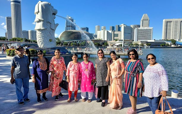 Group of tourists at Merlion Park with Singapore skyline in the background.
