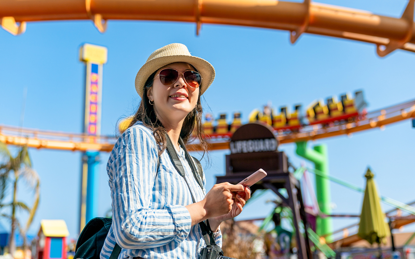 Tourist enjoying a theme park in Singapore with roller coaster in background.