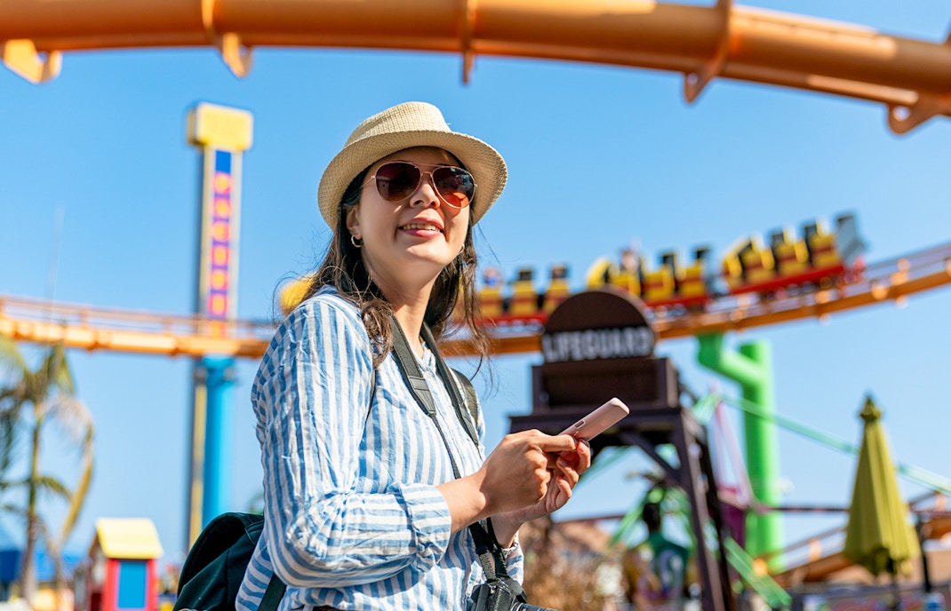 Tourist enjoying a theme park in Singapore with roller coaster in background.