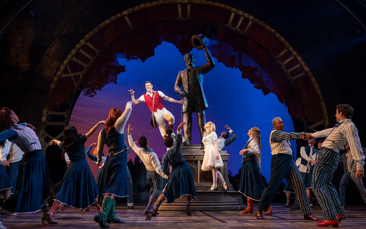 Performers dancing around a statue on stage during a Wicked musical scene.